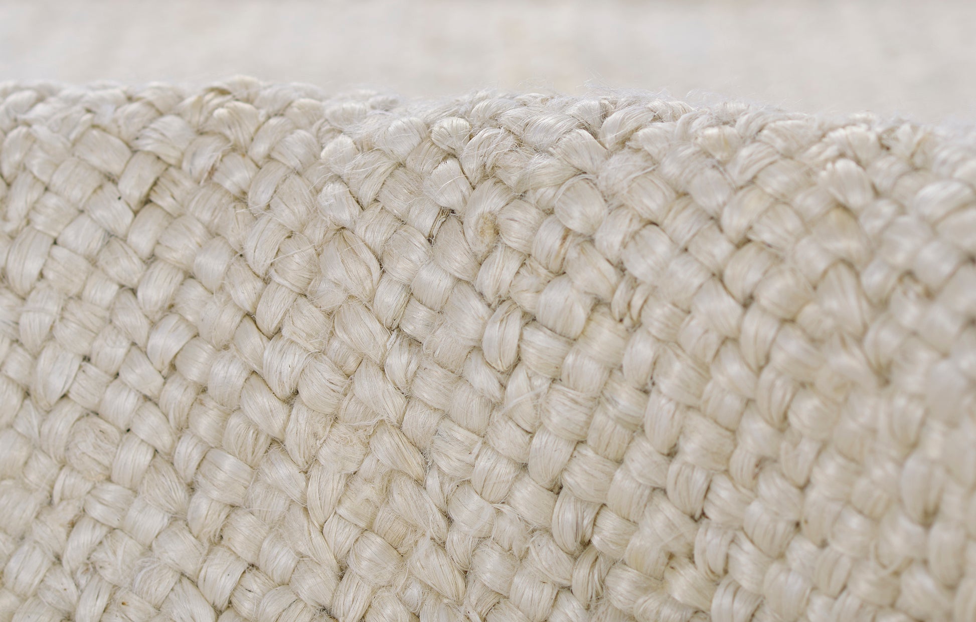 Close-up of cream braided jute weave; thick, chunky fibers create a natural rustic texture for baskets or bags.