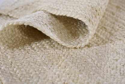 Natural beige jute rug with thick braided weave, rolled edge, rustic natural decor for floors.