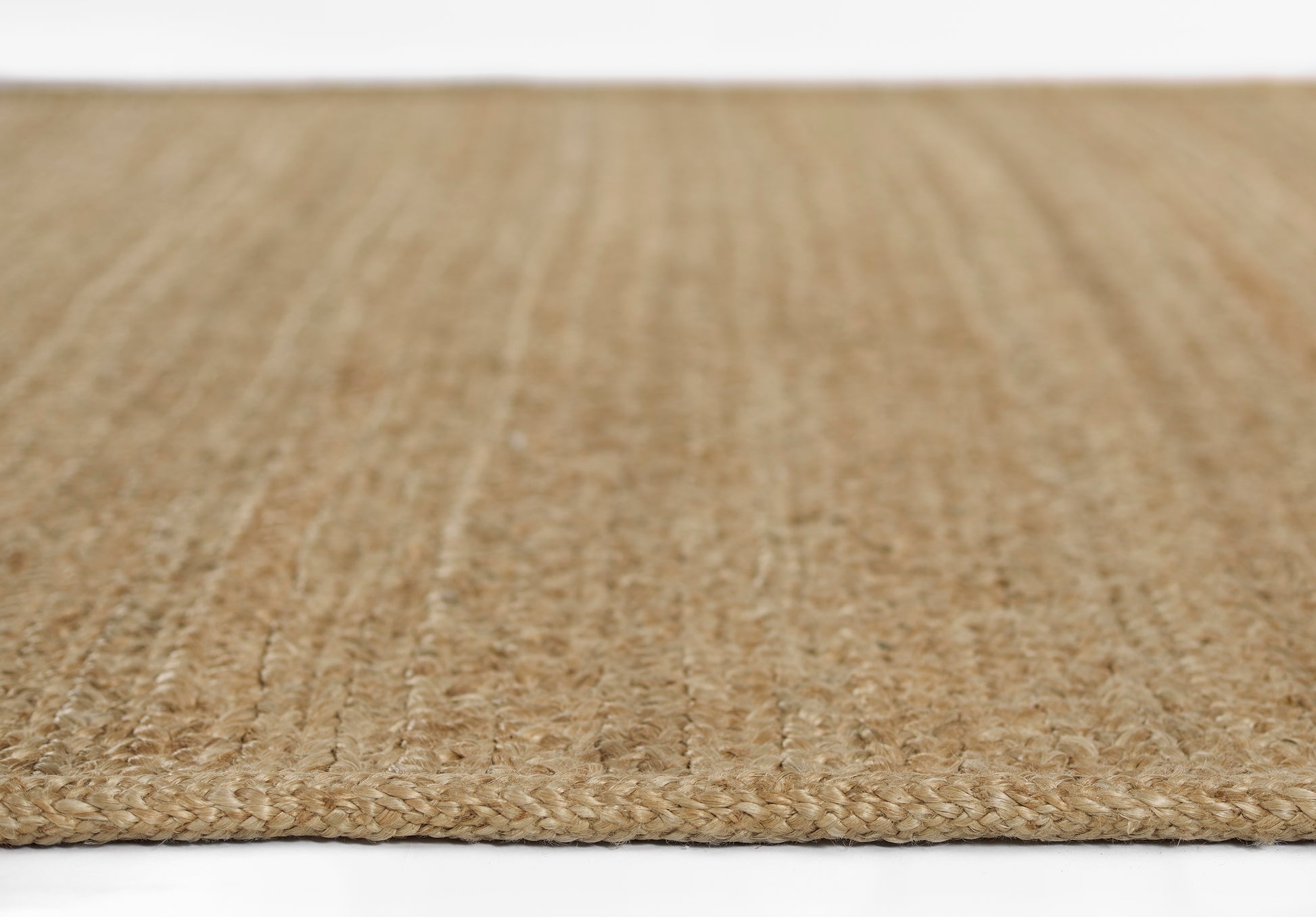 Natural jute rug with braided weave in warm beige tones, close-up edge view.