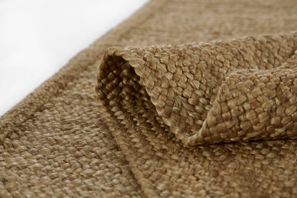 Natural sisal rug in beige-brown braided weave with rolled edge; rustic rectangular floor mat.