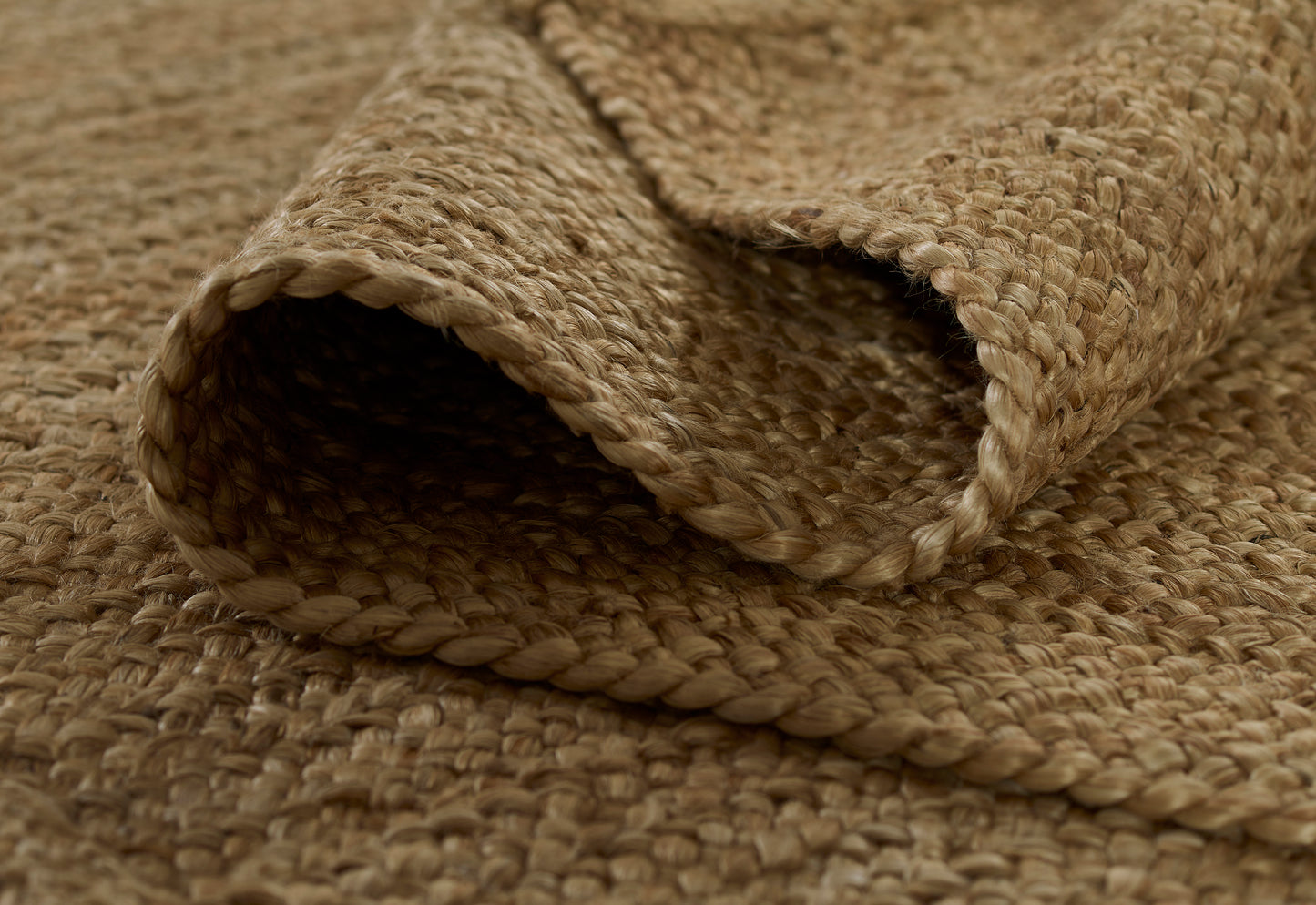Natural jute rug with rolled braided edge, close-up of earthy beige woven texture.