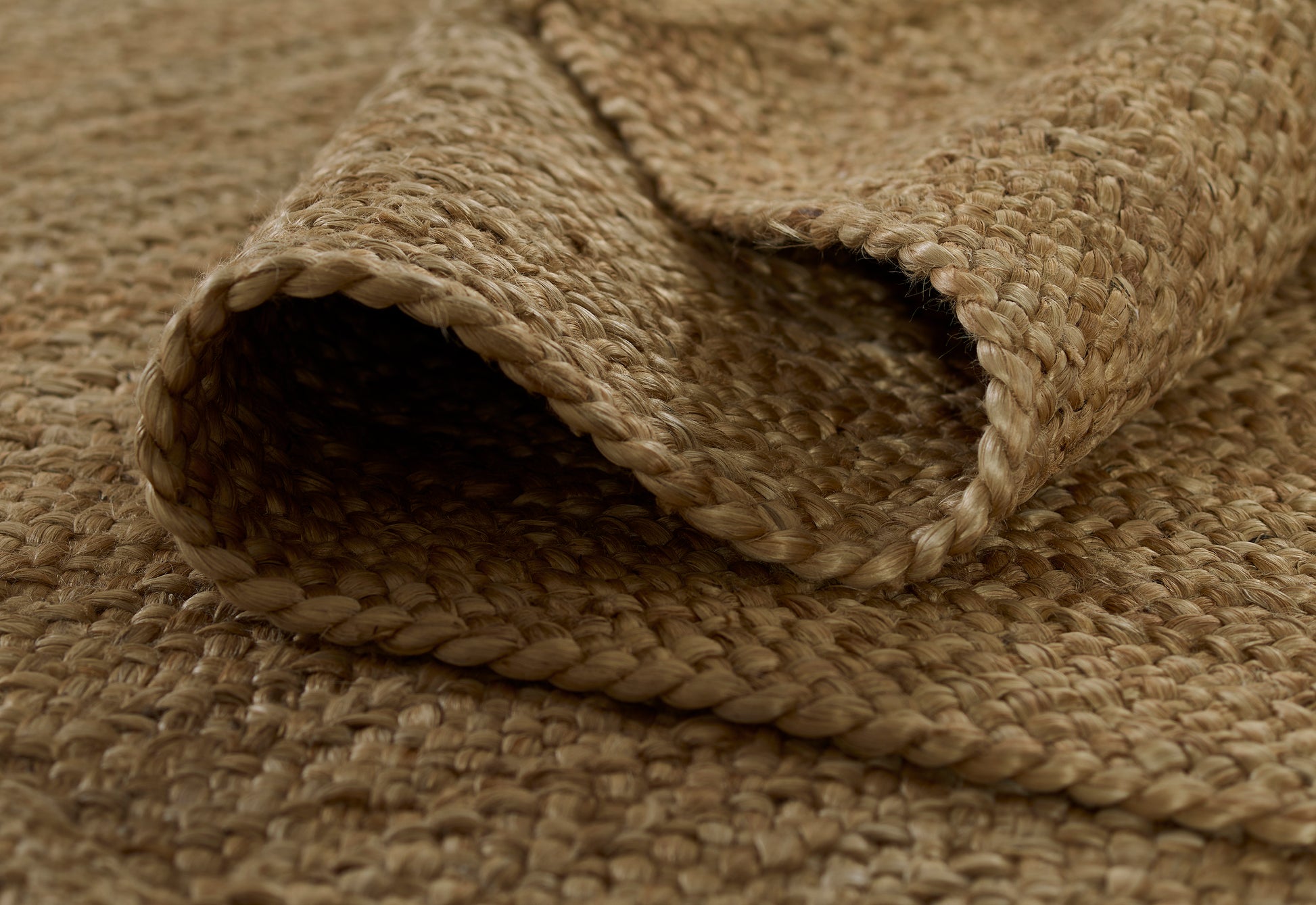 Natural jute woven rug with thick braided fibers in beige-brown tones and rolled edge.
