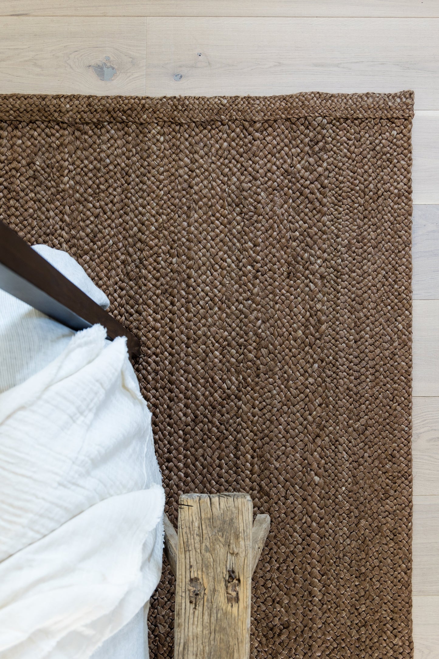 Brown woven jute rug on light wood floor; rustic rectangular area rug beside a bed with white linens.