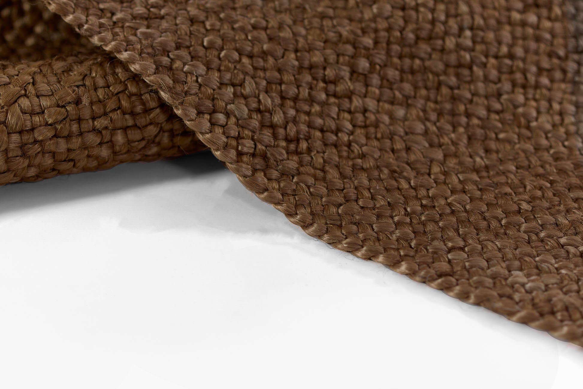 Close-up of a brown natural-fiber woven rug with thick braided texture and curved edge.