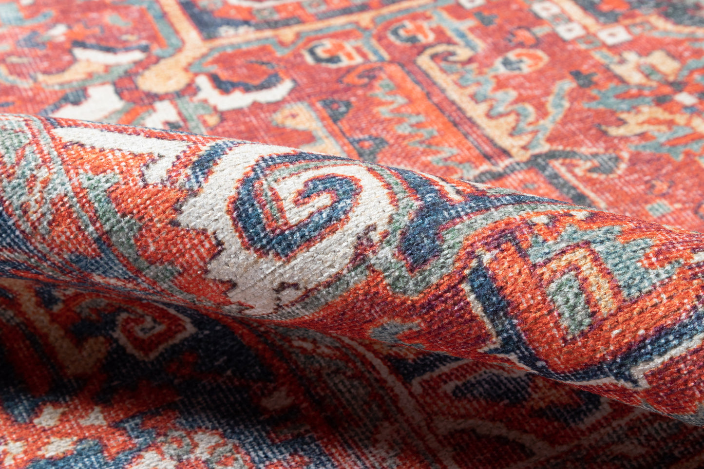 Close-up of a red oriental rug with blue, ivory and teal geometric motifs; woven wool, rolled edge.