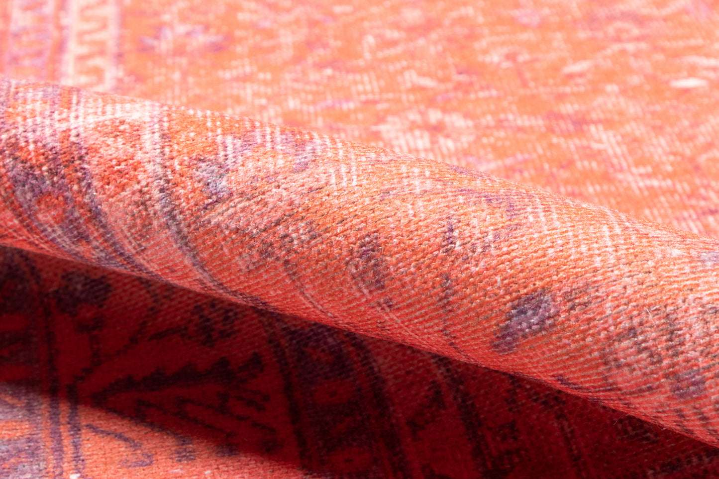 Close-up of orange woven rug with purple geometric pattern and folded edge.