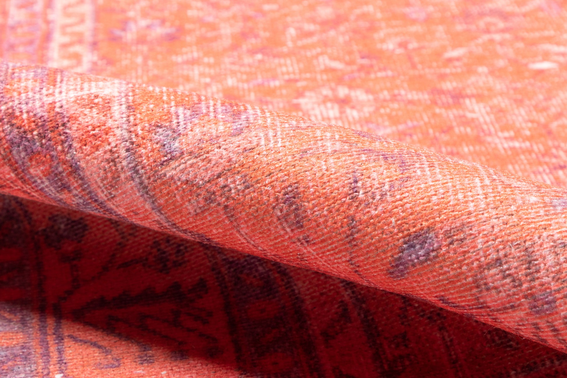 Close-up of orange woven rug with purple geometric pattern and folded edge.