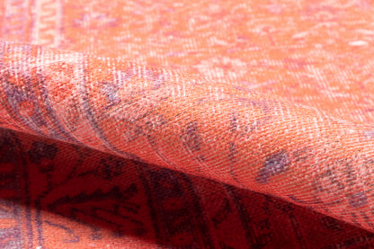 Close-up of orange woven rug with purple geometric pattern and folded edge.