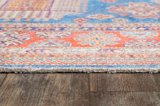 Woven oriental-style rug with blue, orange & cream geometric motifs, fringed edge on dark wood floor.