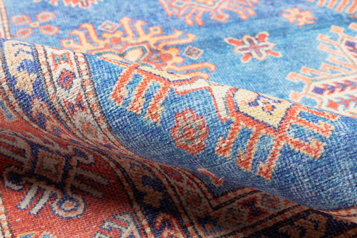 Blue oriental rug with orange and ivory geometric patterns, folded corner view.