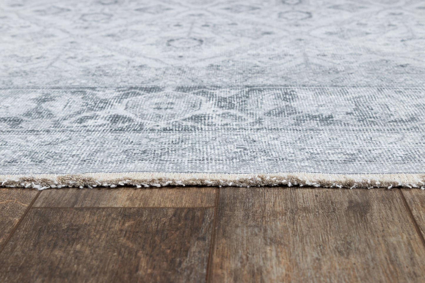 Gray damask-patterned area rug with beige fringe along a dark wood floor.