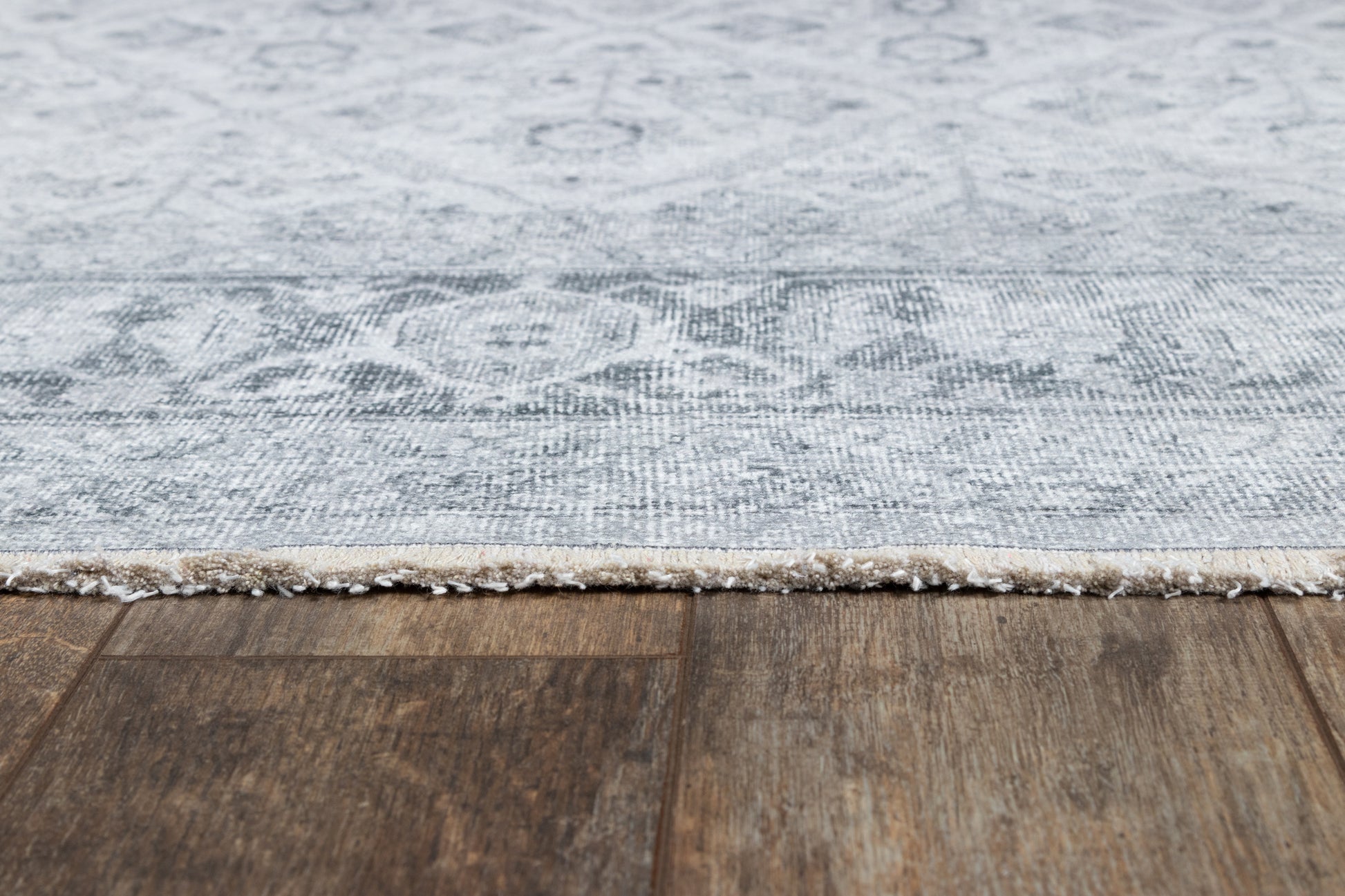 Gray damask-patterned area rug with beige fringe along a dark wood floor.
