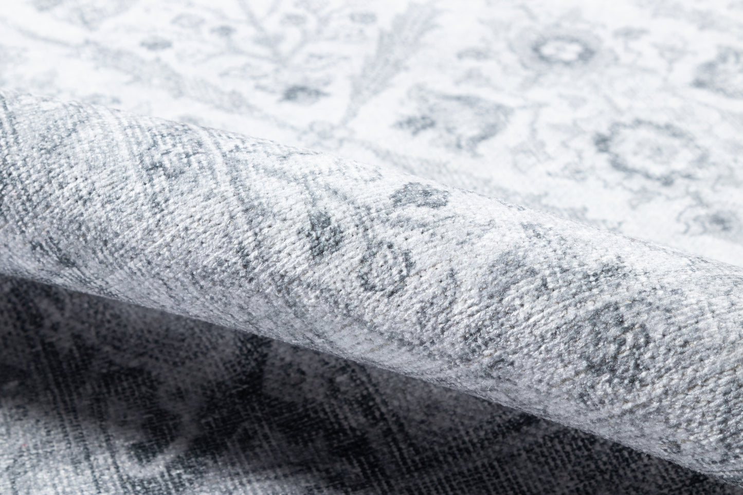 Close-up of light grey distressed floral rug, rolled edge, soft woven texture.