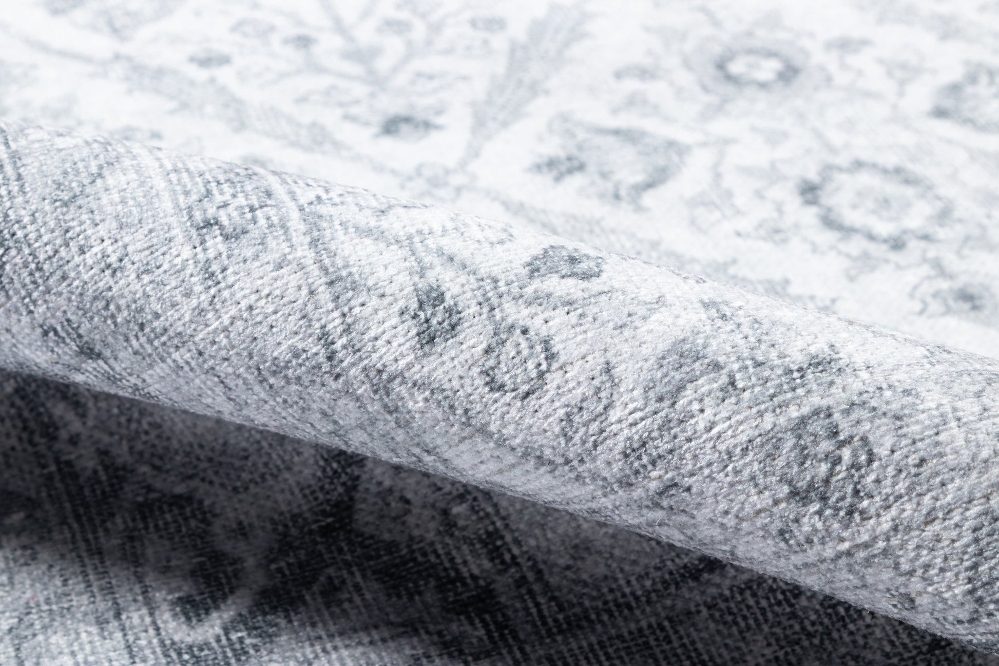 Close-up of light grey distressed floral rug, rolled edge, soft woven texture.