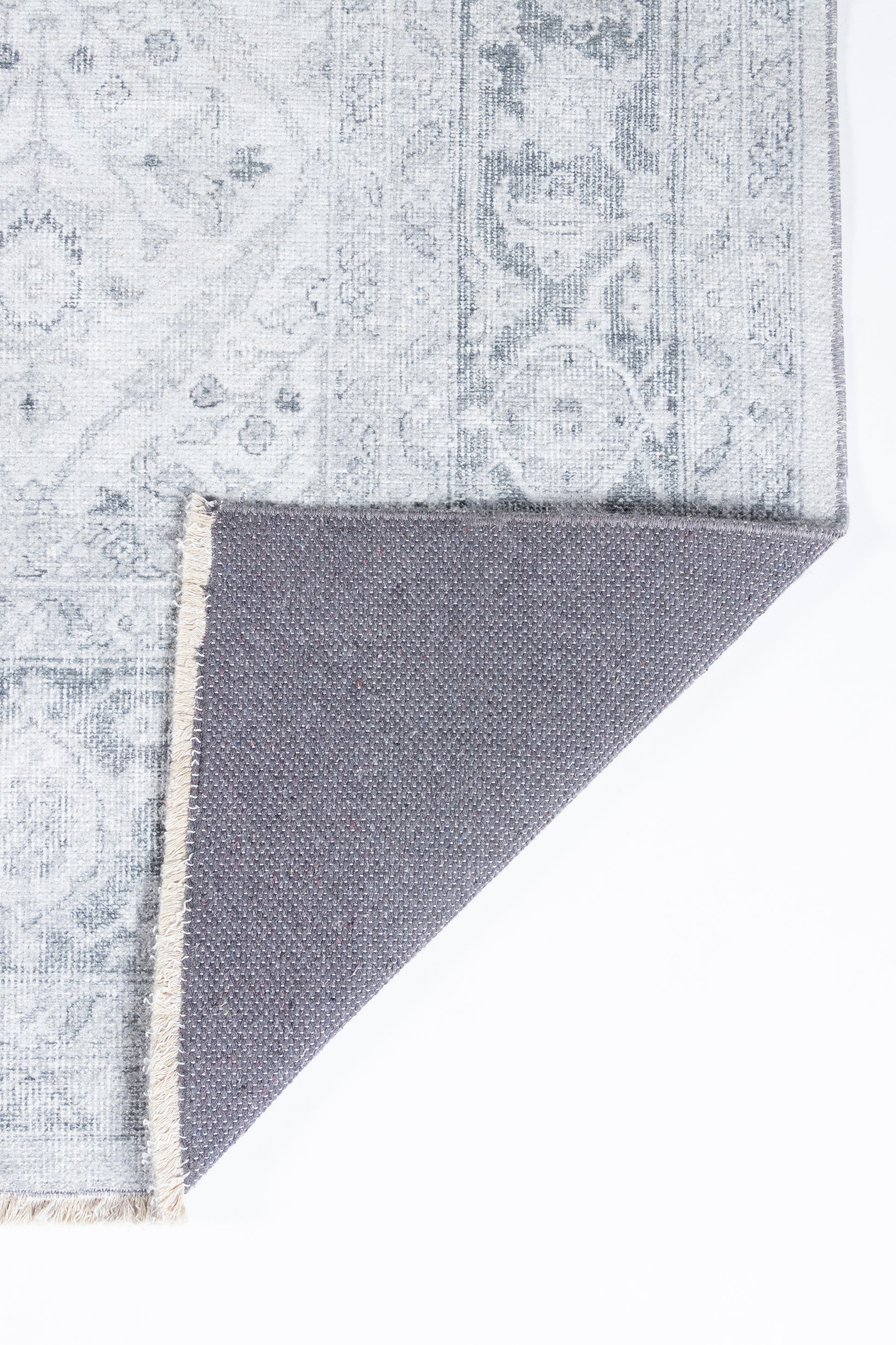 Gray patterned rug with vintage floral motif, blue-gray tones, folded corner reveals darker reverse weave.