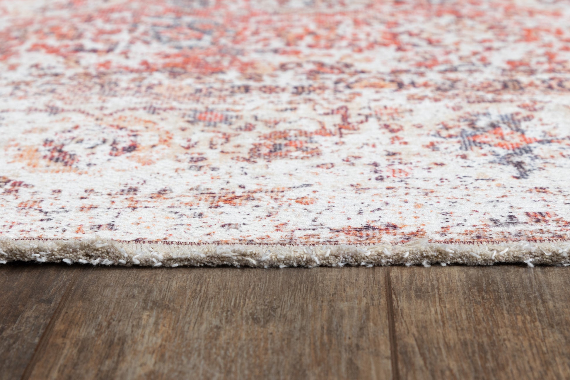 Red and ivory distressed patterned area rug with fringed edge on dark wooden floor