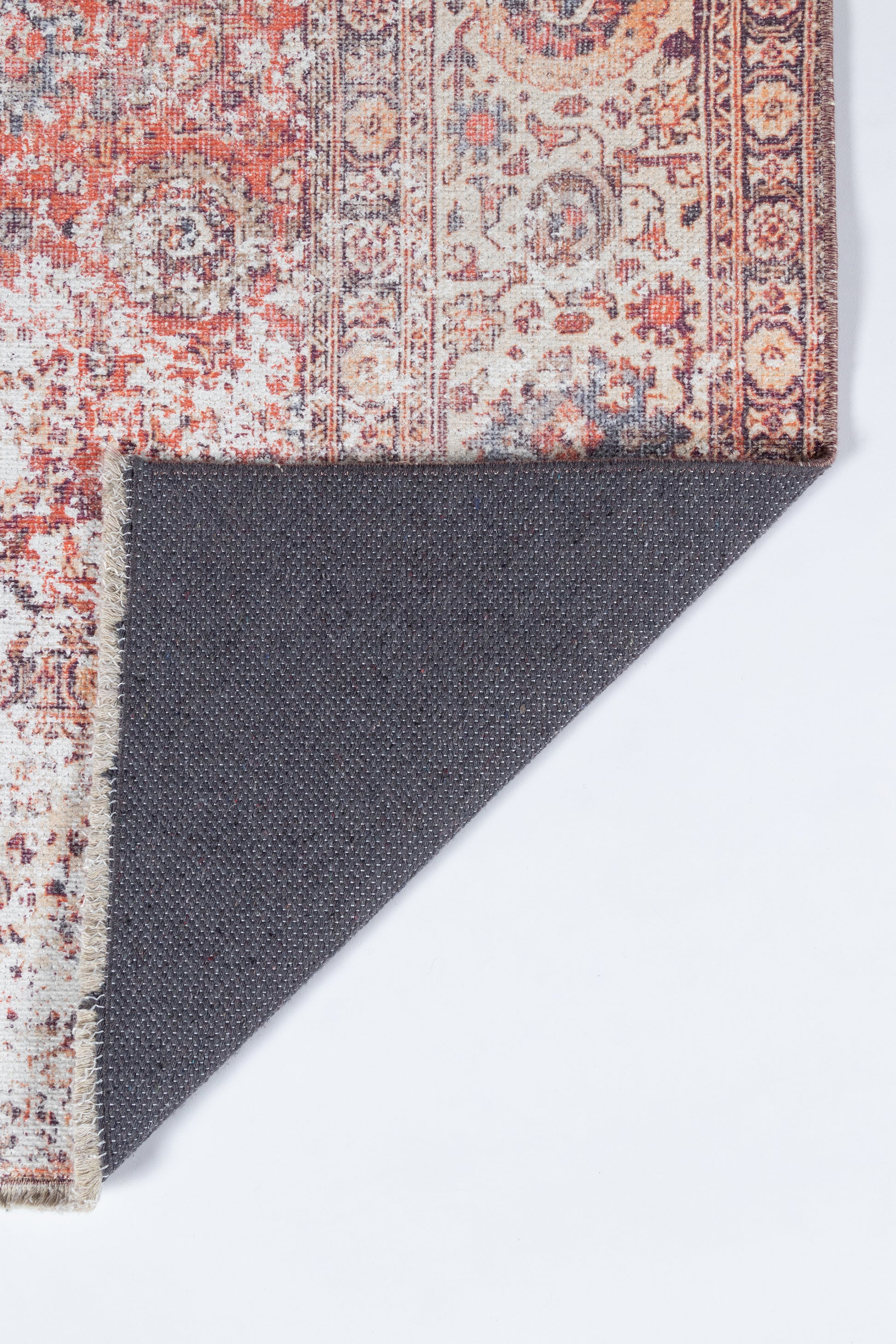 Persian-inspired rug in red, ivory and cream with intricate motifs; corner folded to reveal dark gray backing