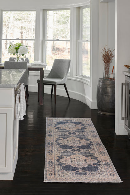 Navy and ivory patterned rug on dark hardwood in a bright white kitchen with gray upholstered dining chairs.
