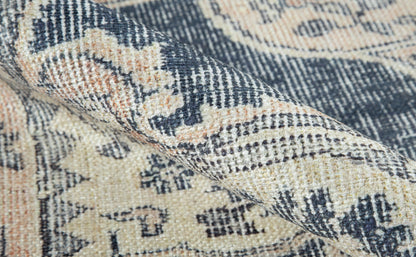 Close-up of a beige and navy woven rug with cream and peach accents, ornate floral pattern and textured pile.