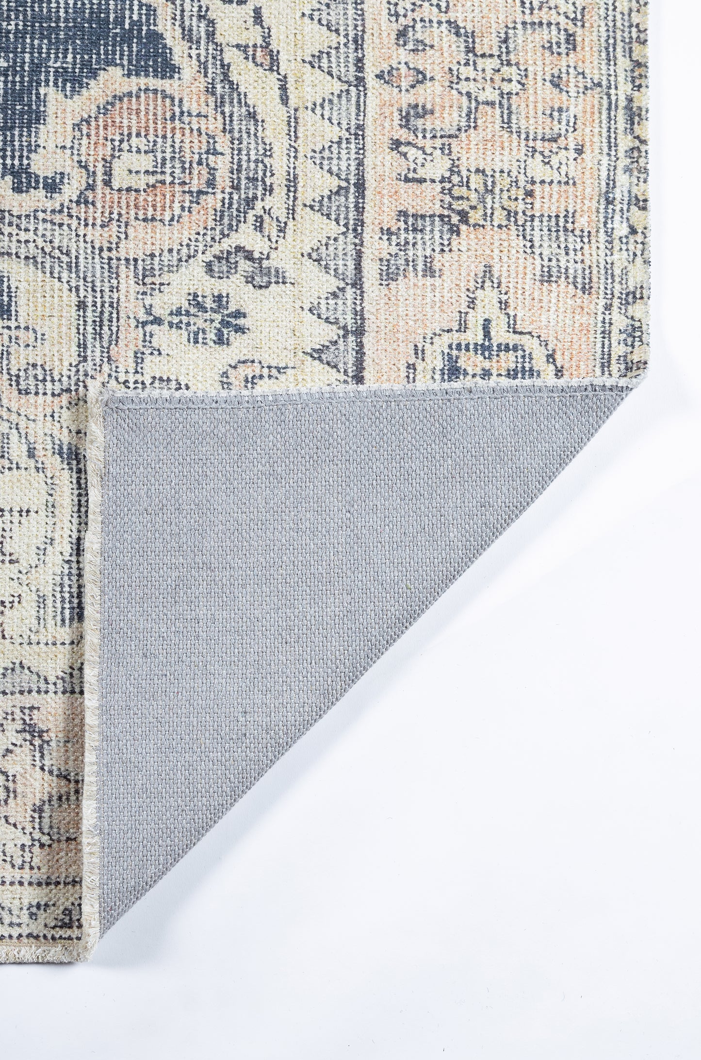 Ornate patterned rug in navy, cream and peach with floral motifs; folded corner reveals grey non-slip backing.