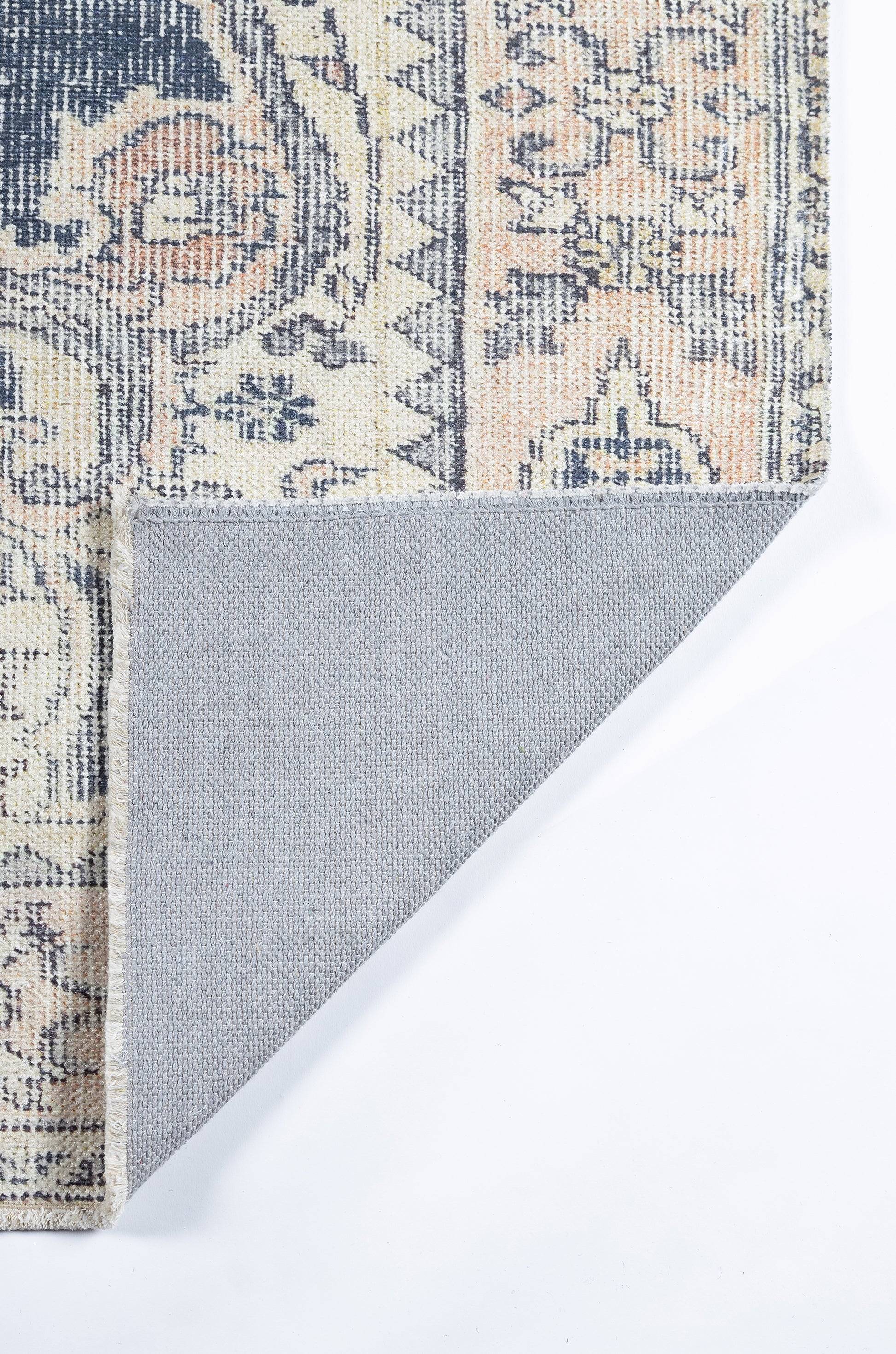 Ornate patterned rug in navy, cream and peach with floral motifs; folded corner reveals grey non-slip backing.