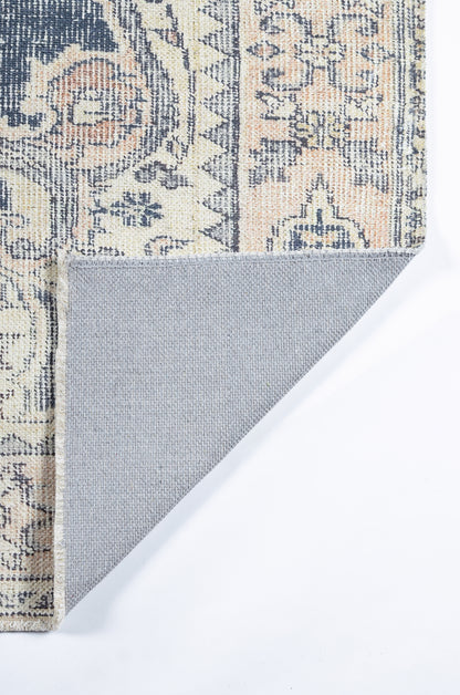 Ornate patterned rug in navy, cream and peach with floral motifs; folded corner reveals grey non-slip backing.