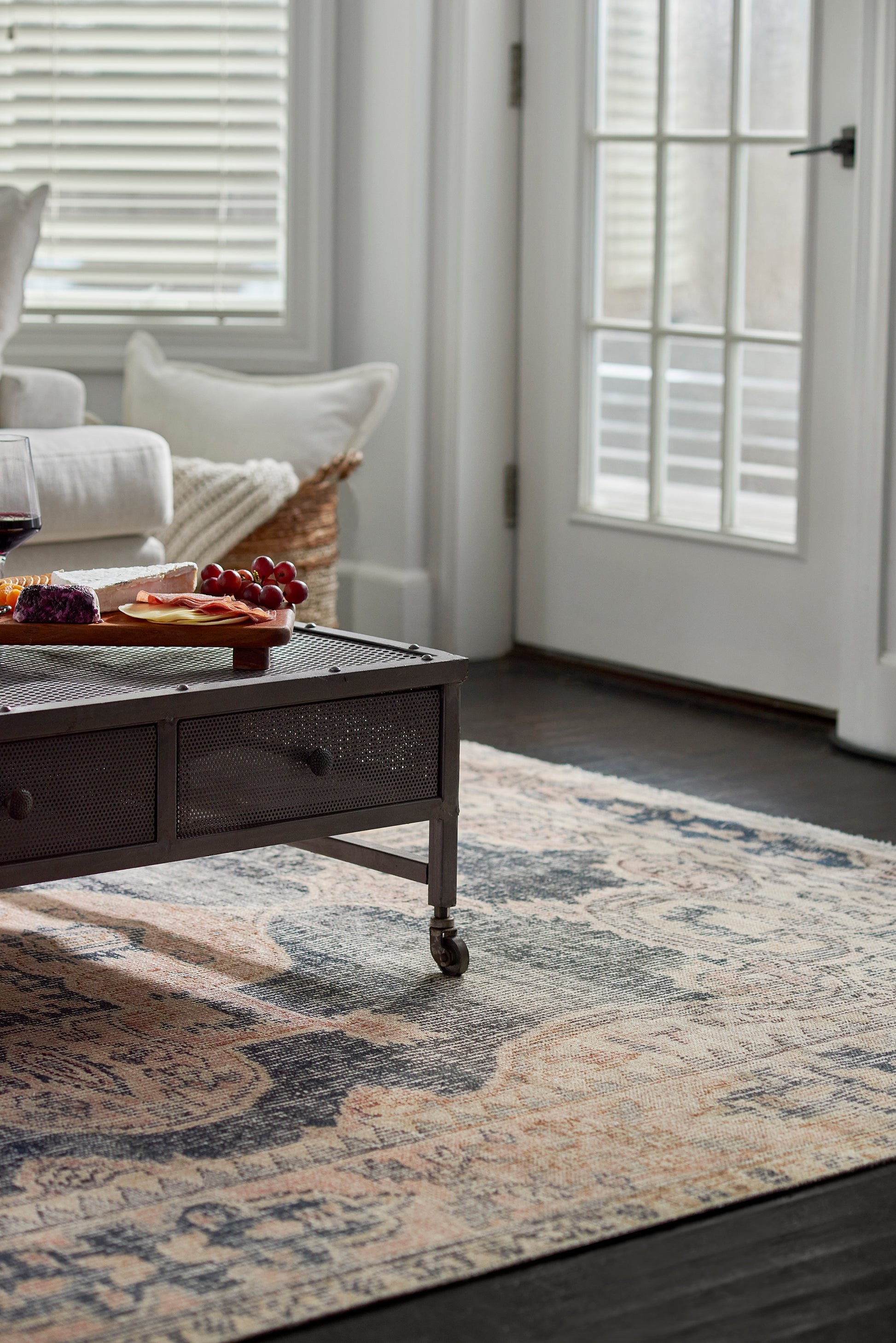 8' x 10' Oriental rug in a cozy gray living room, with a dark metal coffee table featuring mesh drawers & wheels holding a cheese board, grapes, and wine.