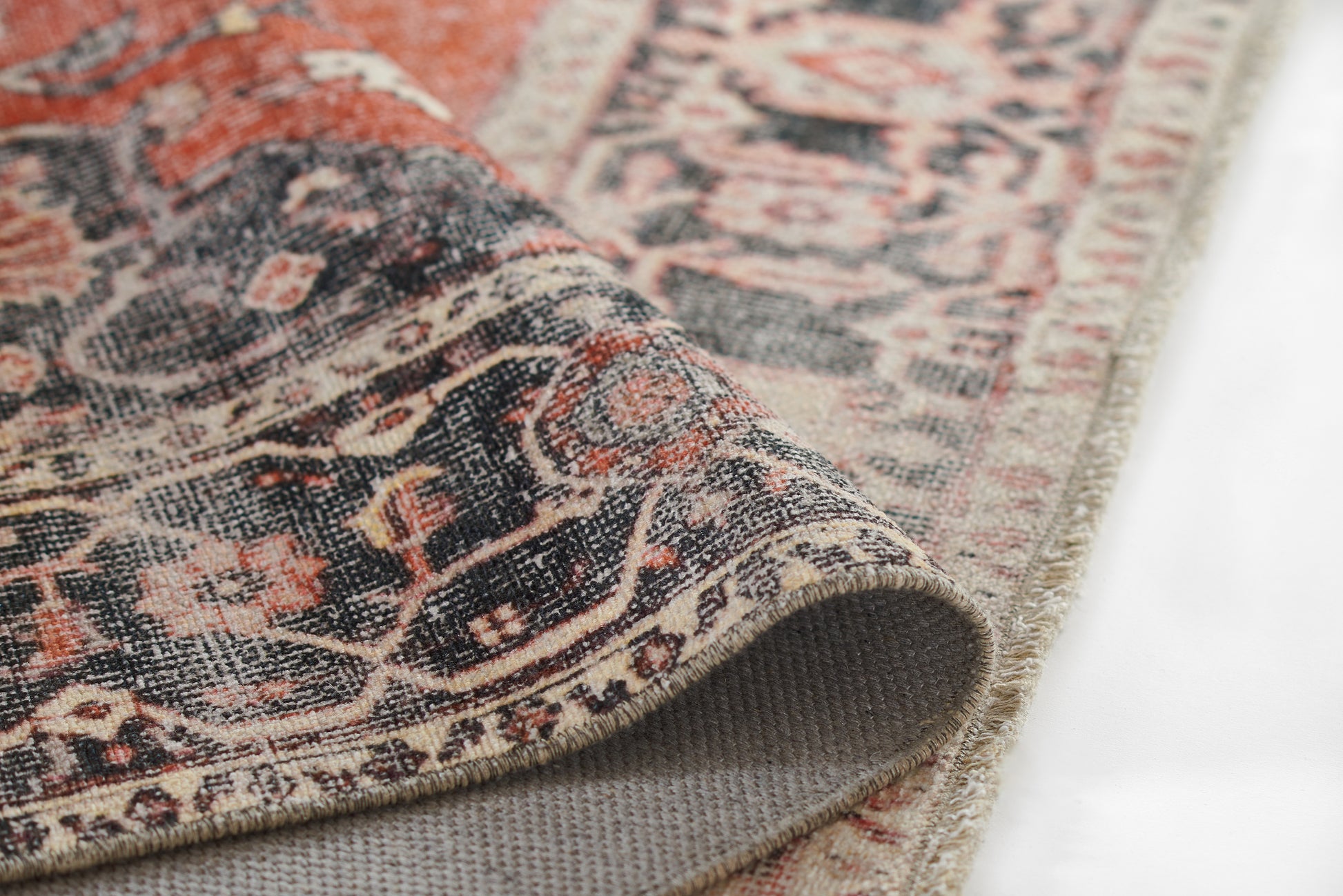 Close-up of a Persian-style rug with red, cream and navy tones, intricate floral border, folded corner.