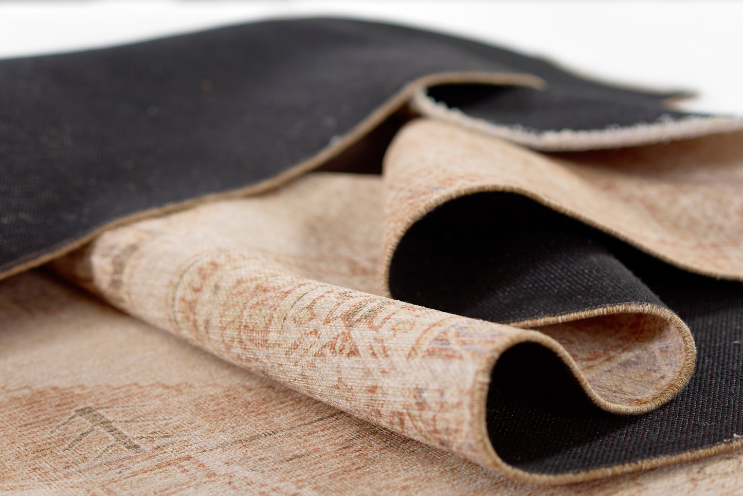 Beige patterned rug with a textured weave and curved folds.