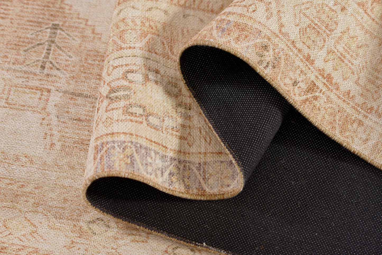 Beige Persian-style runner rug with subtle rust motifs, rolled back to reveal a black textured non-slip backing.