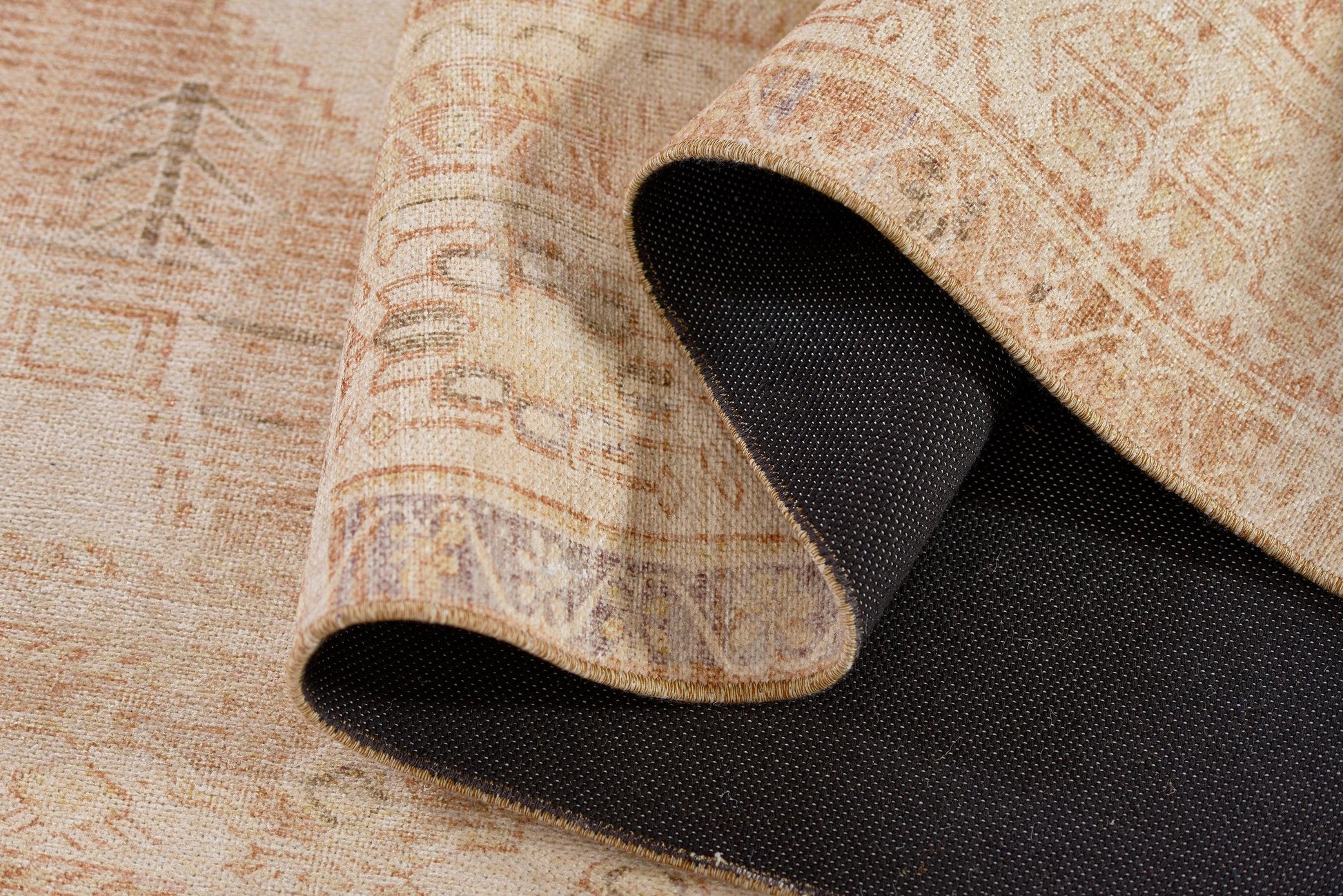 Beige oriental rug with peach and tan motifs; rolled corner reveals dark textured backing.