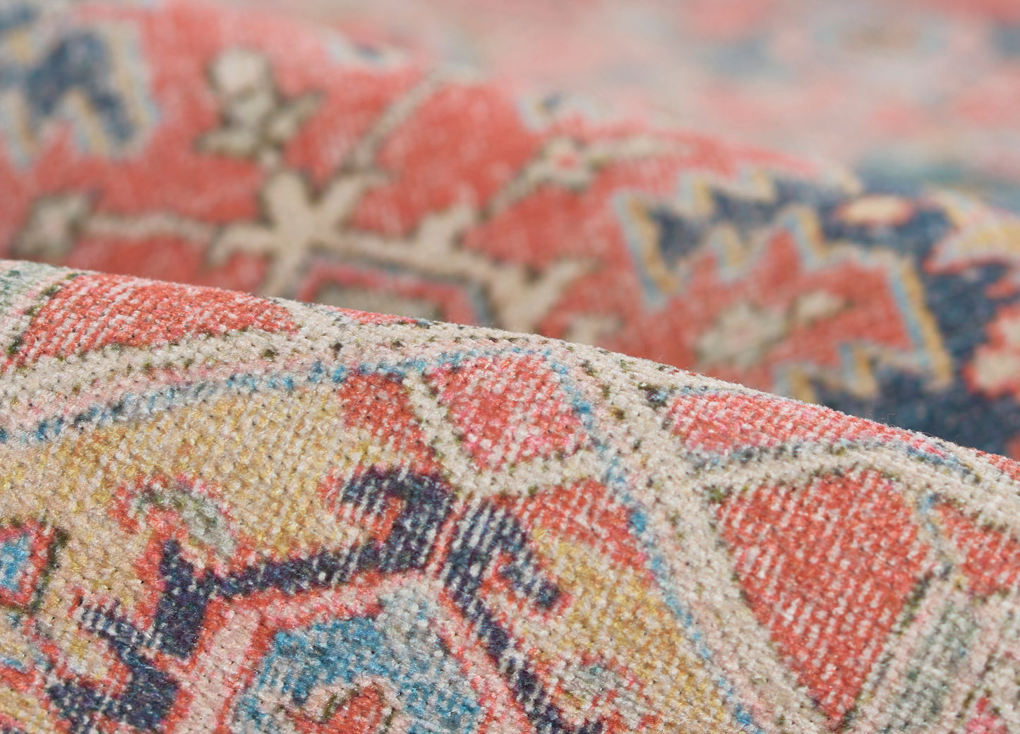 Close-up of a textured woven rug in red, blue, ivory and gold with geometric motifs.