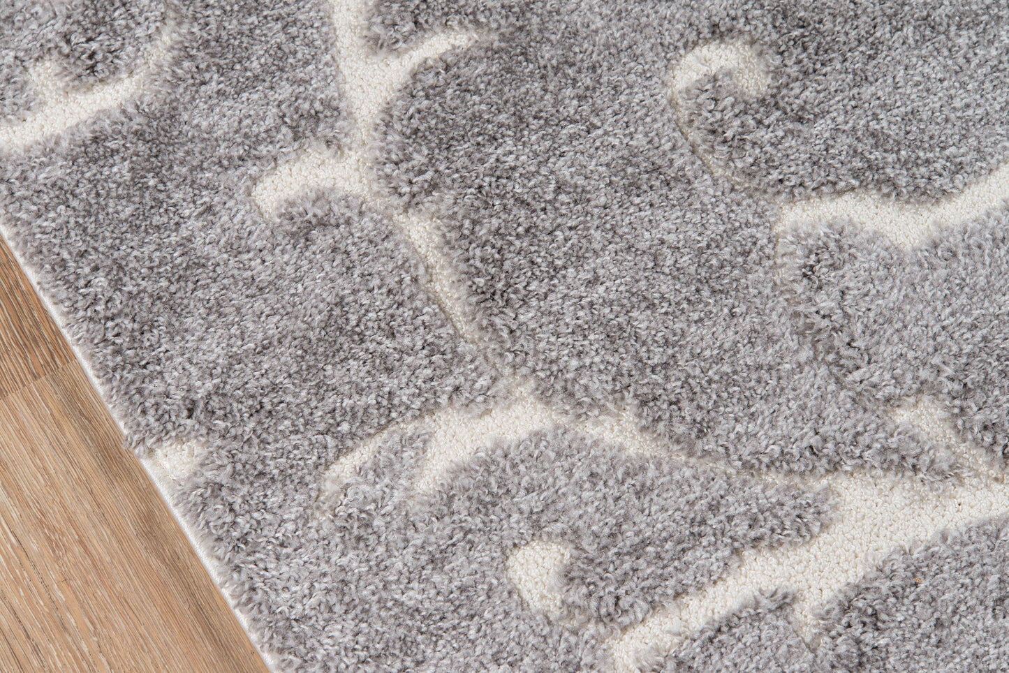 Gray shag rug with ivory abstract curved pattern on wood floor.