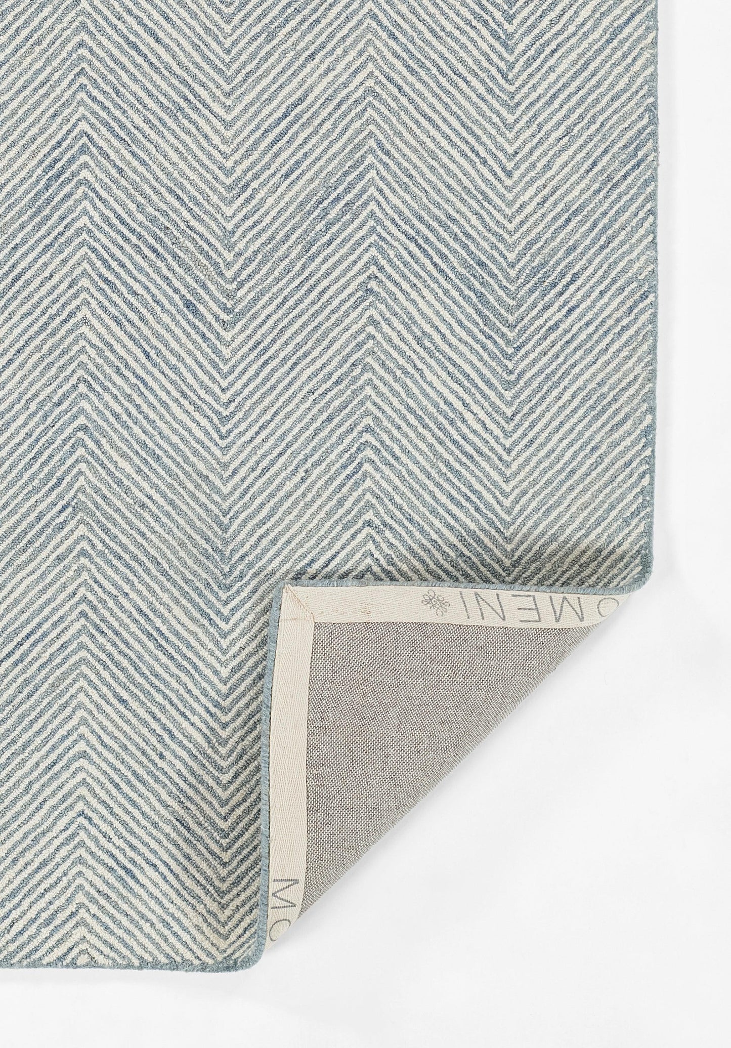 Blue chevron-pattern woven rug sample with light beige underside; folded corner reveals the backing.