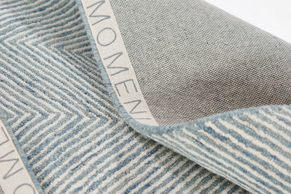 Blue chevron-striped woven rug, soft textured yarns, folded edge with light grey reverse and white branded trim.