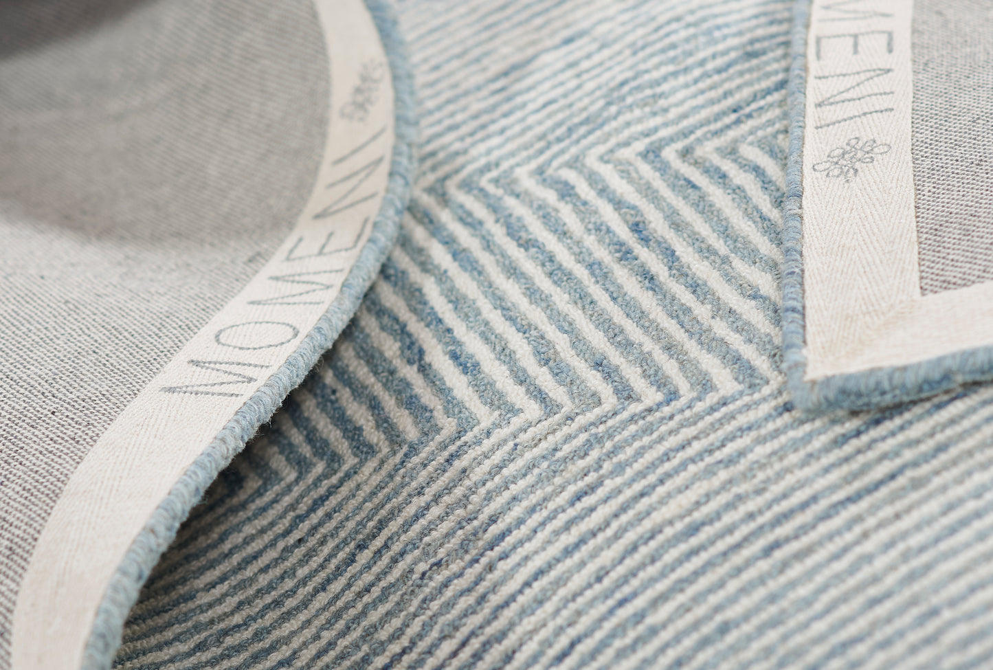 Close-up view of light blue striped denim texture with white woven trim and small label patch.