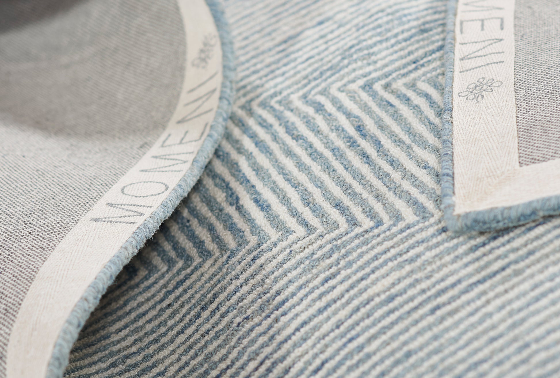 Close-up view of light blue striped denim texture with white woven trim and small label patch.