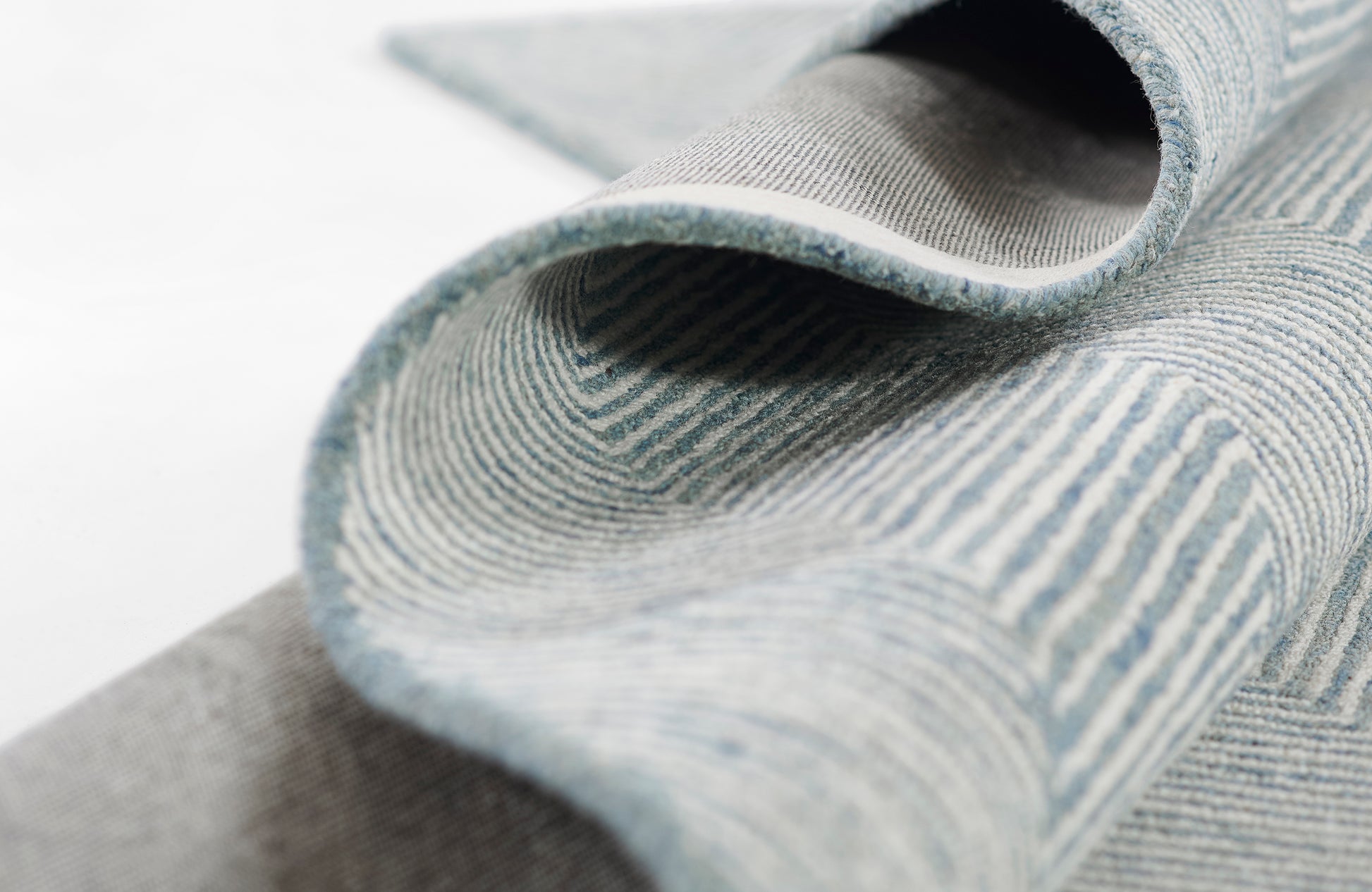 Blue-gray striped woven rug rolled open to reveal soft textured pile and curved edge.