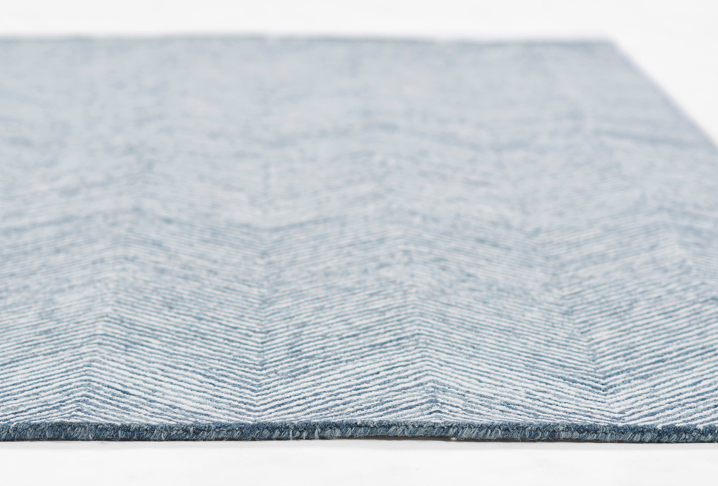 Blue chevron-patterned woven rug with a fringed edge and soft textured weave.