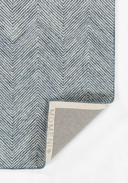 Blue and white chevron-weave rectangular rug, folded corner shows beige backing and edge label.