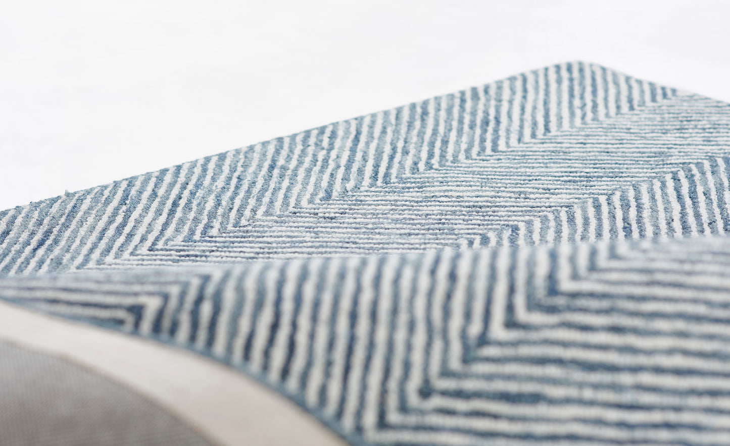 Blue and white chevron-striped woven textile, close-up fold; versatile throw or rug.