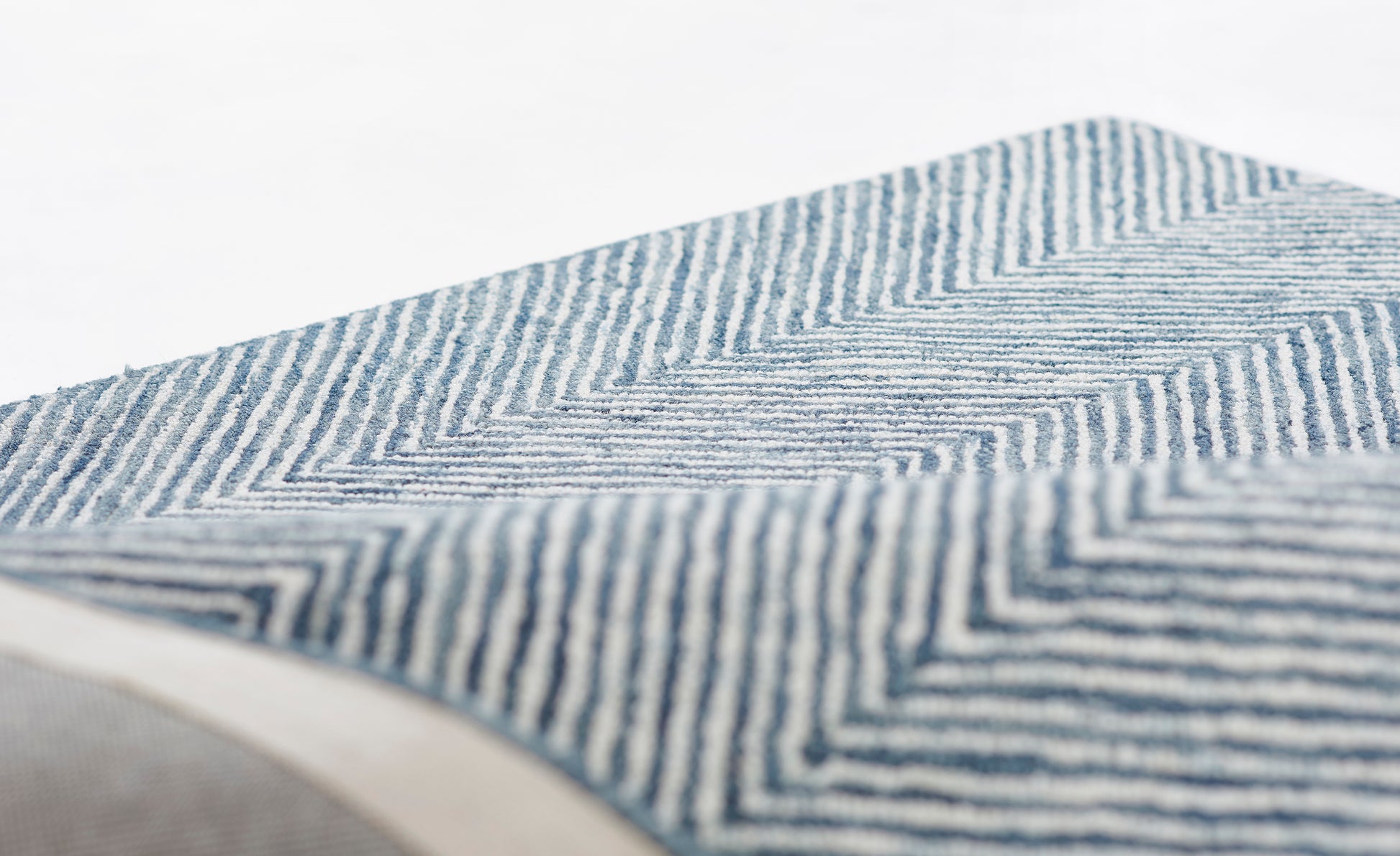 Blue and white chevron-striped woven rug with a rolled edge, close-up texture.