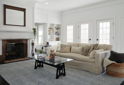 Bright neutral living room with beige sofa, glass coffee table, blue-gray striped rug, white fireplace & built-in shelves.