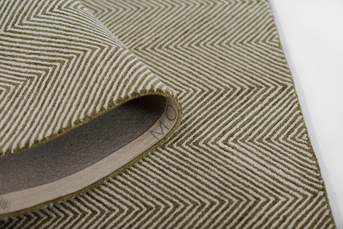 Olive & cream chevron herringbone woven rug, rolled edge showing beige underside.