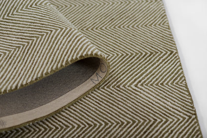 Olive green chevron woven rug with beige zigzag stripes, folded to reveal gray backing and tan edge.