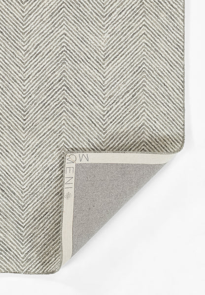Gray chevron woven rug, with light cream binding; folded corner reveals gray underside and textured surface.