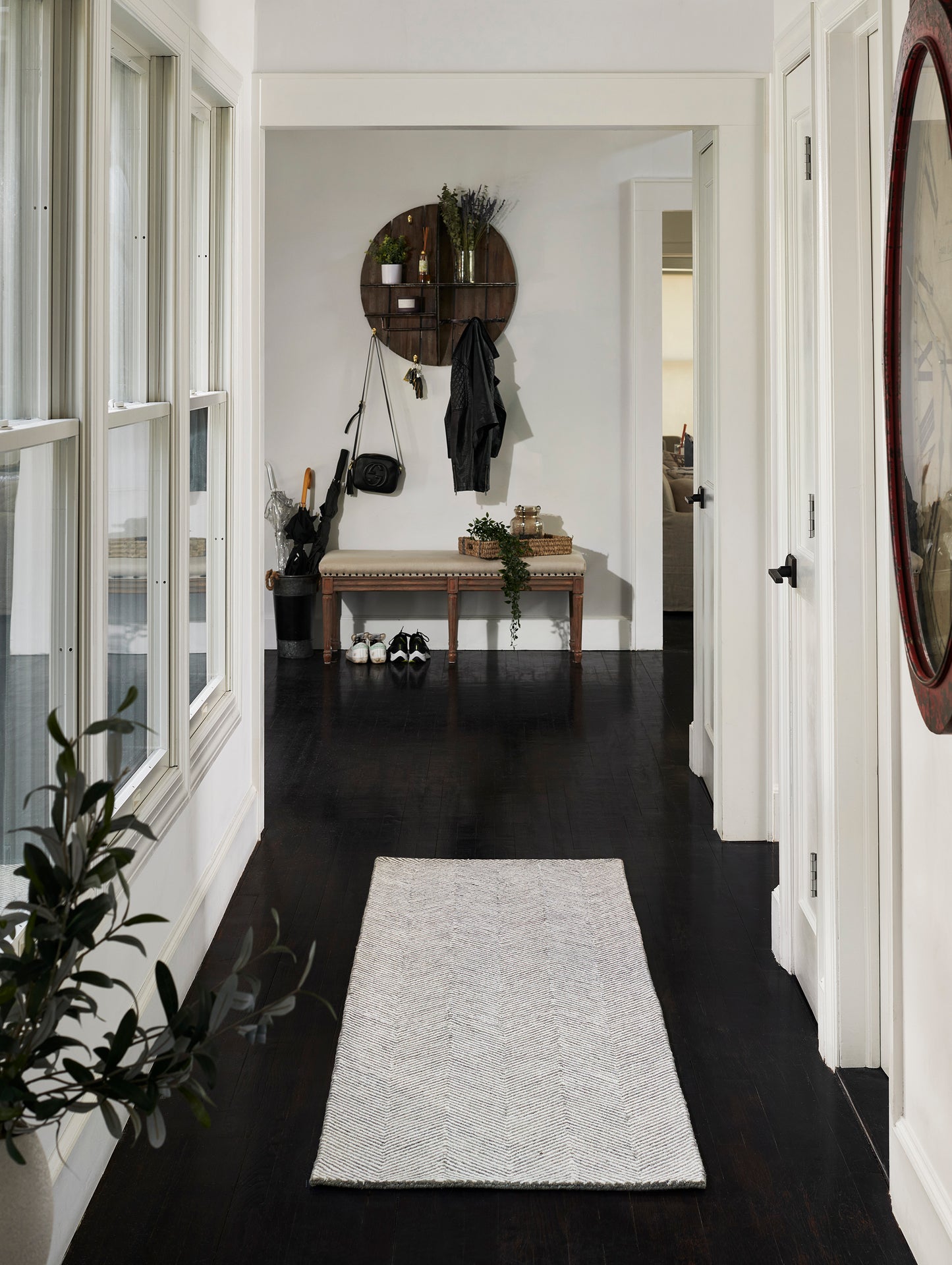 Light gray textured runner rug on dark hardwood hallway with bench and circular wall shelf in background.