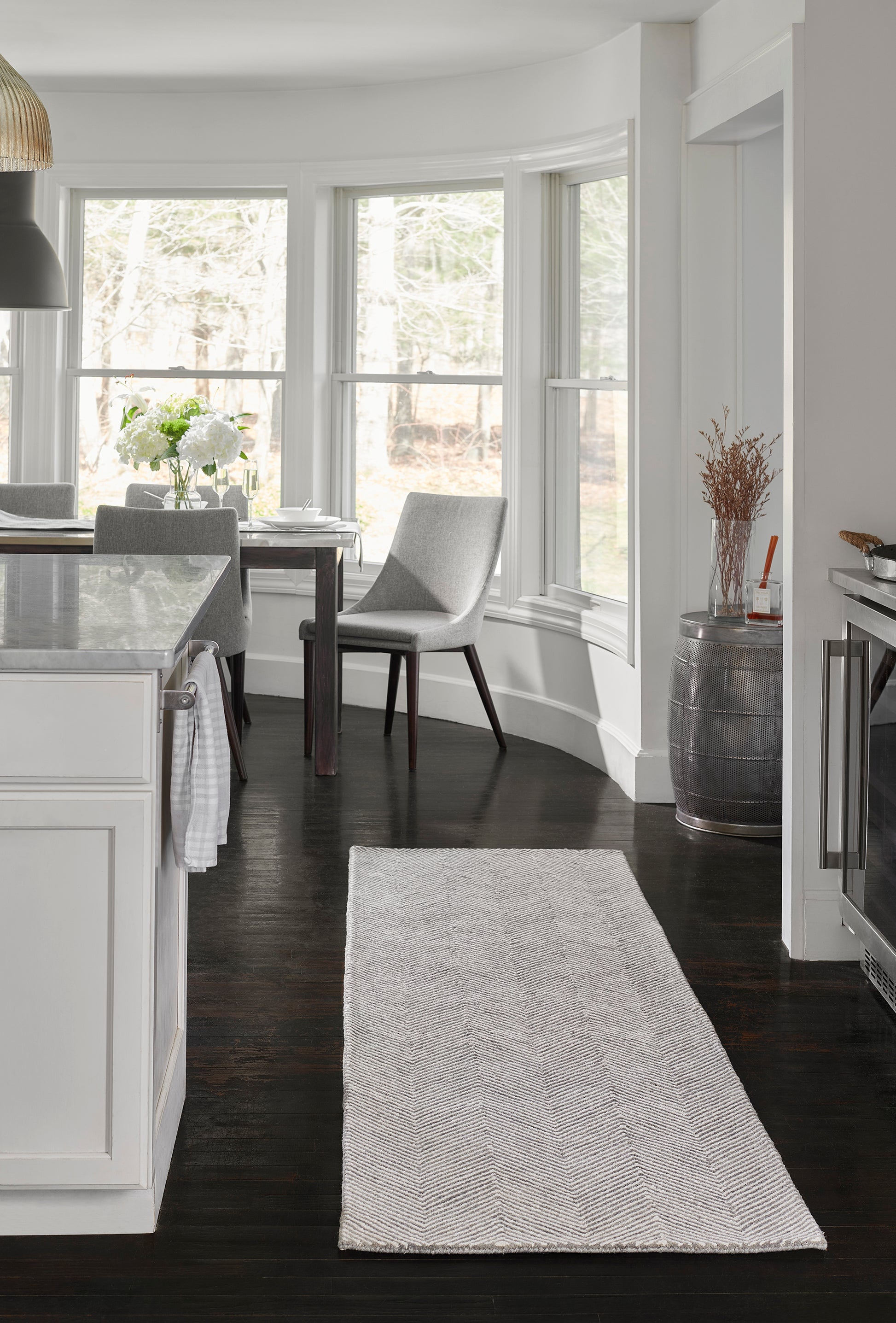 Long gray chevron rug on dark wood floor in a modern white kitchen and dining area.