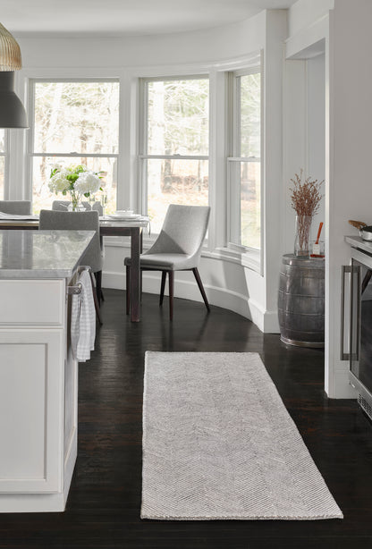 Long gray chevron rug on dark wood floor in a modern white kitchen and dining area.