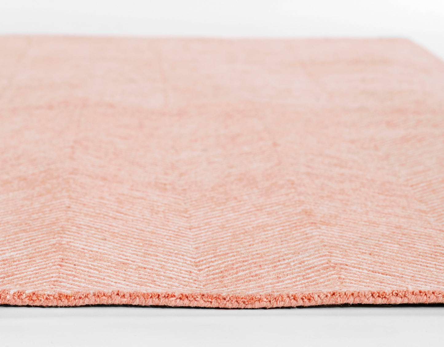 Peach-pink chevron-patterned rug with plush pile and stitched edge, close-up texture.